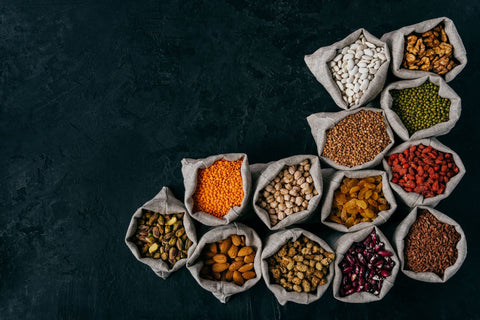 A horizontal image of small sacks filled with almonds, walnuts, raisins, and garbanzos on a black background, prepared for freeze-drying.