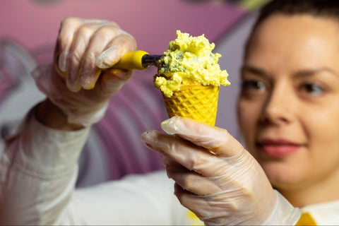 A woman scooping ice cream into a waffle cone.
