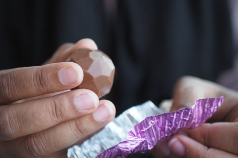 A delicious-looking chocolate candy emerges as a man peels away the foil wrapper.