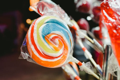 Brightly colored lollipop wrapped in plastic with other candies in the background.
