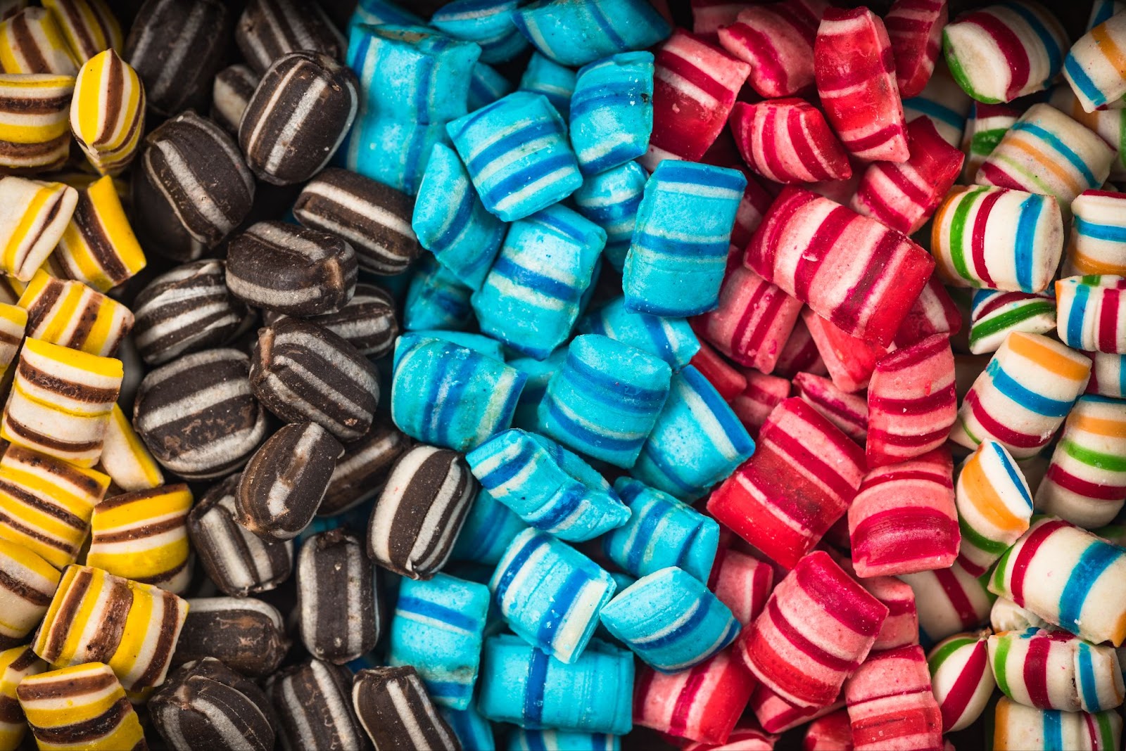 A vibrant display of assorted striped candies in red, yellow, brown, blue, red and white, arranged to showcase their unique and colorful patterns.