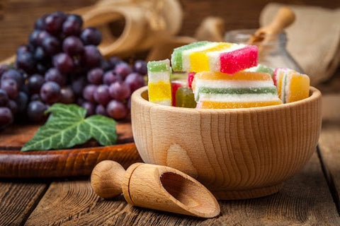 Colorful jelly candies are displayed in a wooden bowl against a wooden background, creating an enticing and visually appealing treat.