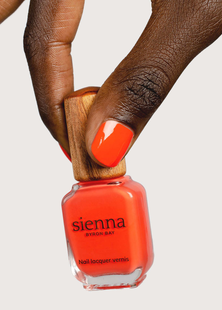 Dark brown skin tone holding and wearing Tango orange nail polish