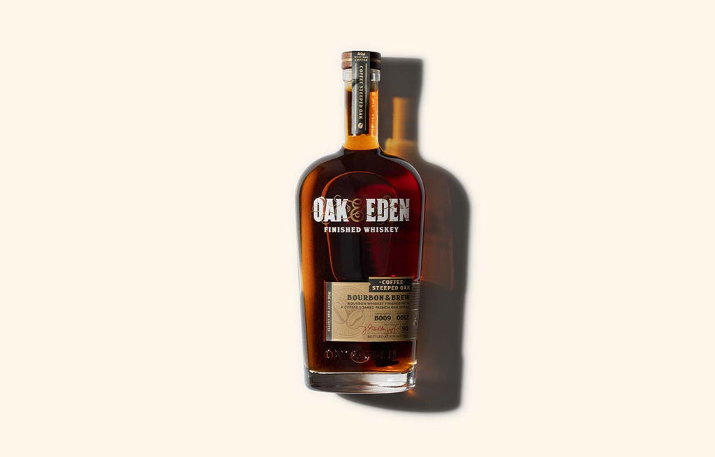 A bottle of Oak & Eden Bourbon & Brew. Cold brew coffee infused bourbon. It is laying on a flat surface with a hard shadow pushing to the right of the bottle.