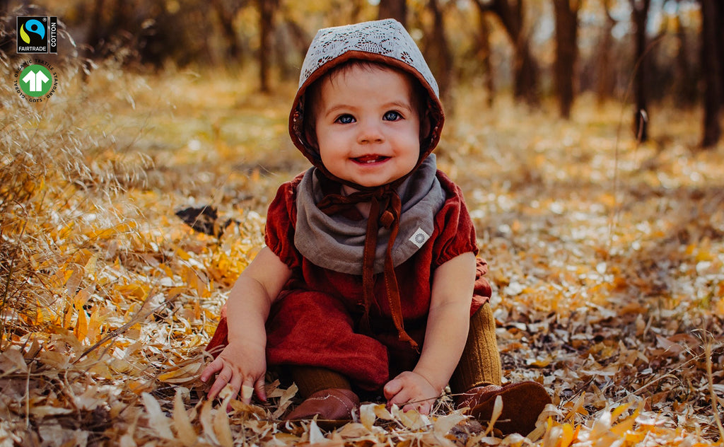 smiling baby girl sitting down in open field wearing organic olive Infinity bib