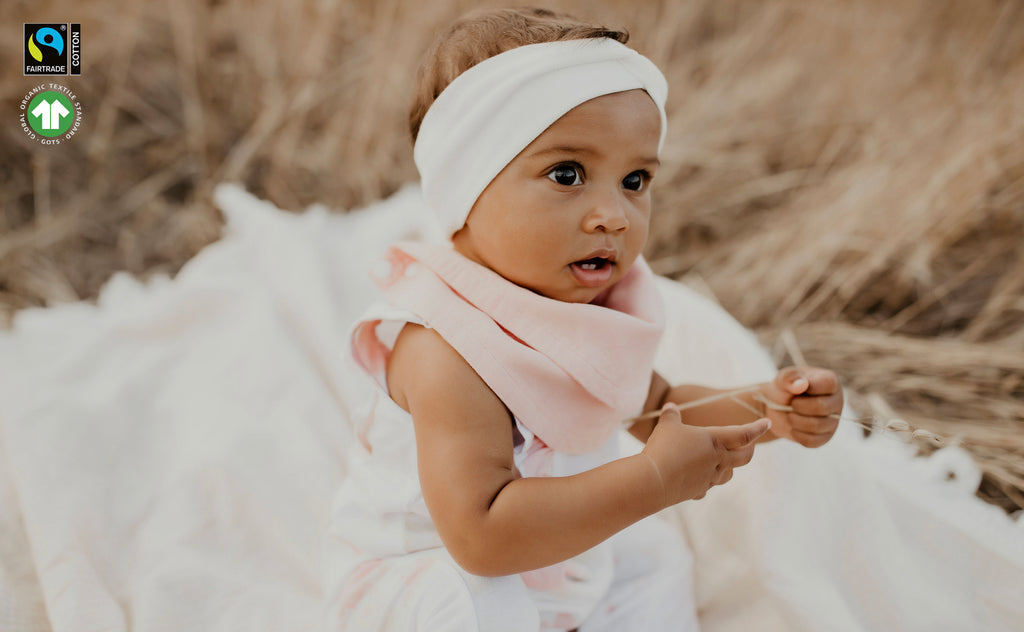 baby girl sitting on a white blanket in an open field wearing peach Infinity bib