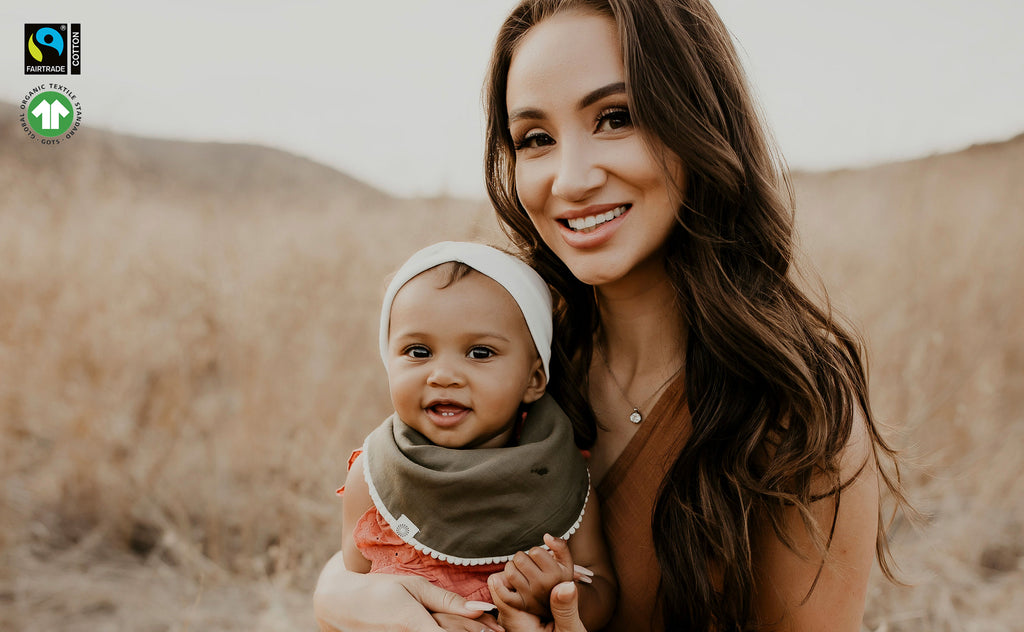 mom holding baby girl in open field - baby wearing dark olive pom pom bib