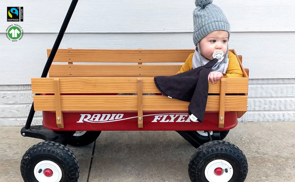 toddler baby boy riding in Radio Flyer wagon while sucking on pacifier attached to charcoal paci blanket