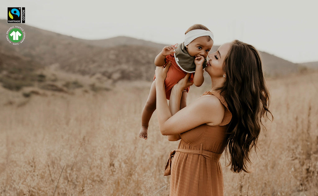 mom holding up baby girl in open field - baby wearing dark olive pom pom bib