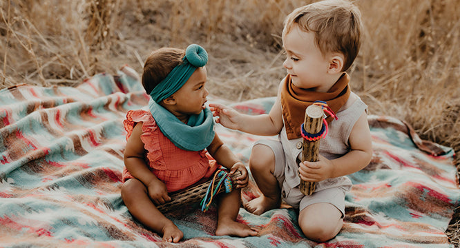 baby girl and toddler boy sitting on blanket in open field wearing Indi By Kishu Baby muslin bibs