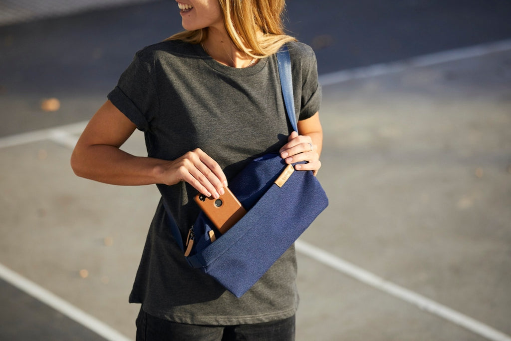 White female stands in a parking lot slipping a cell phone into their crossbody City Pouch by Bellroy