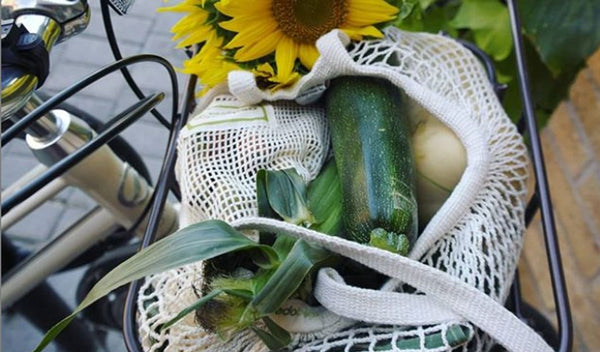 Reusable material string market bag from the brand Credobags carrying fresh produce and vibrant yellow sunflowers on the front of a bicycle