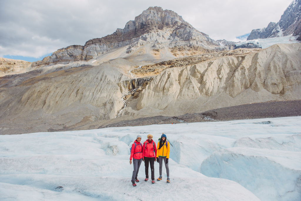 Three BIPOC hikers stand smiling in front of a wintery mountainscape on Canada's west coast