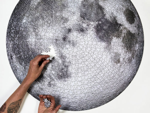 Two hands piecing together Four Point Puzzles' circular moon puzzle