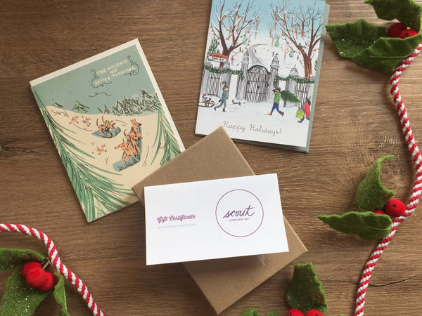Flat lay of two holiday cards and a Scout gift certificate on a wooden backdrop with a festive rope decorated with felt mistletoe