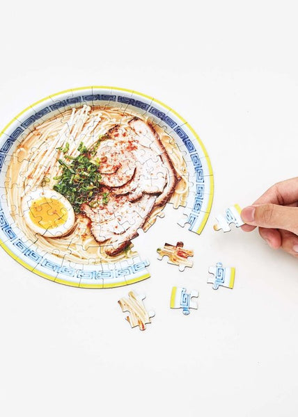 A hand working on a round ramen puzzle 