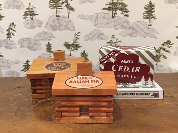 Paine incense cabins sit on a bench in front of a wallpaper featuring an outdoor scene inspired by the Canadian Shield