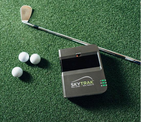 The Original Skytrak Launch Monitor is placed on a hitting mat surrounded by golf clubs and balls. The setup suggests a practice or training environment, with the Skytrak ready to capture swing data. The scene is characterized by a mix of golfing equipment, creating a setup suitable for honing golf skills and tracking performance.