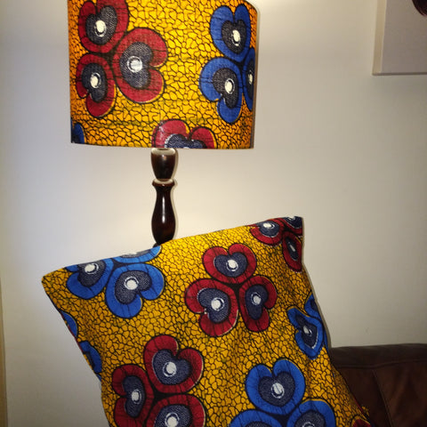 Matching African wax print fabric floor lampshade and cushion. They have vibrant red blue flowers on an earthy gold colourway.