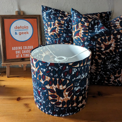 Dark blue with wine red & orange botanical pattern lampshade with two matching cushions. There is a display sign in the background with the "Detola & Geek" logo on it as well as the quote "Adding colour one shade at a time".