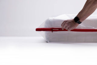 a side shot of a mans hand opening the zipper on a queen mattress bag with a queen mattress inside