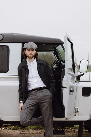 A man leaning on a Land Rover and wearing a Christys' 8 Piece Baker Boy Tweed Cap