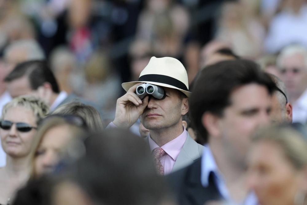 A man in a racing audience looking through binoculars