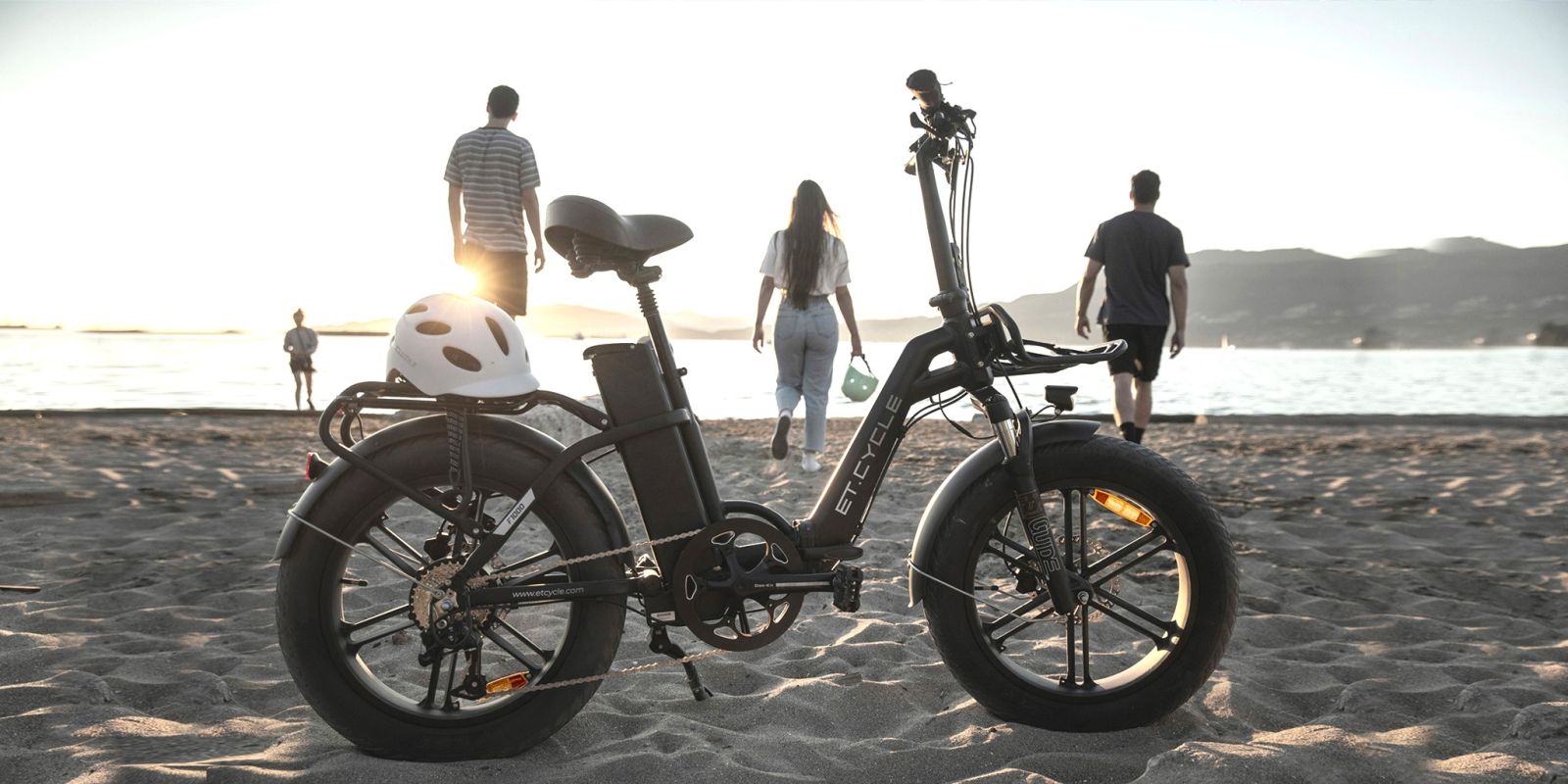 F1000 EBike Sitting on the Sand on a Beach with People and Water in the Background