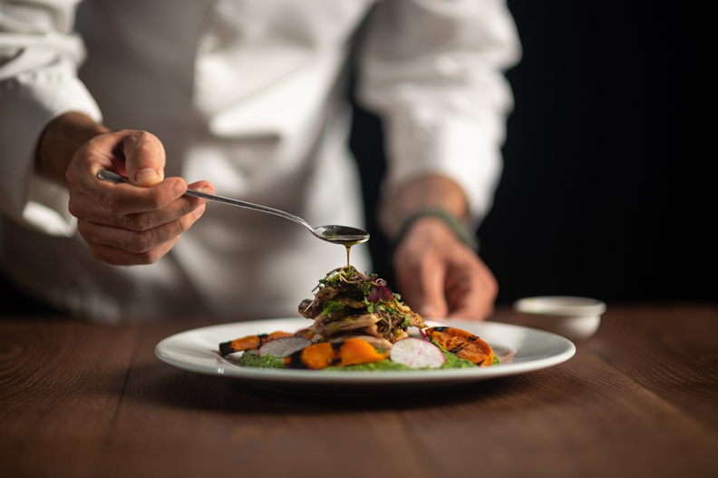 A person pouring a spoon of dressing onto a plate of salad