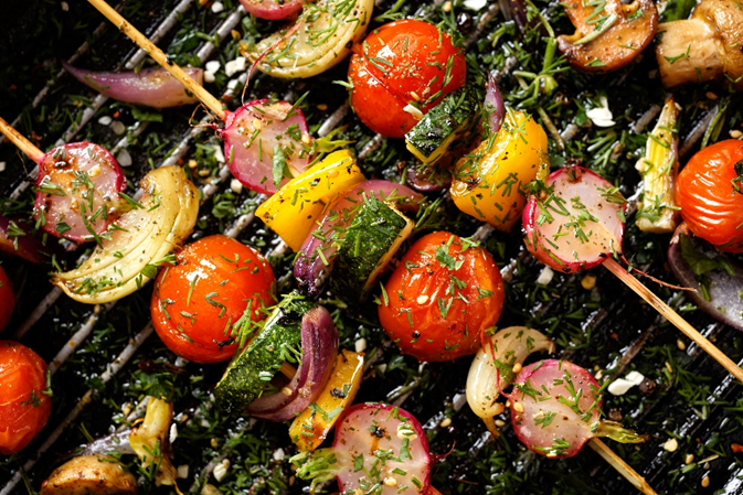 Vegetables such as tomatoes, peppers and onions on skewers on a grill