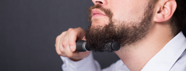 Bearded man using a small round brush to style his beard