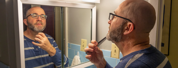Man combing his beard in the bathroom mirror
