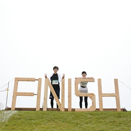 「FINISH」と書かれたゴールで記念撮影をする参加者、カメラにピースを向けている
