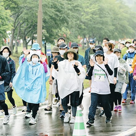 雨天の中、3人の参加者がカメラに向かって手を振っている