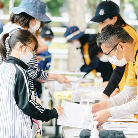 子供の来場者と書類の受け渡しをするボランティア