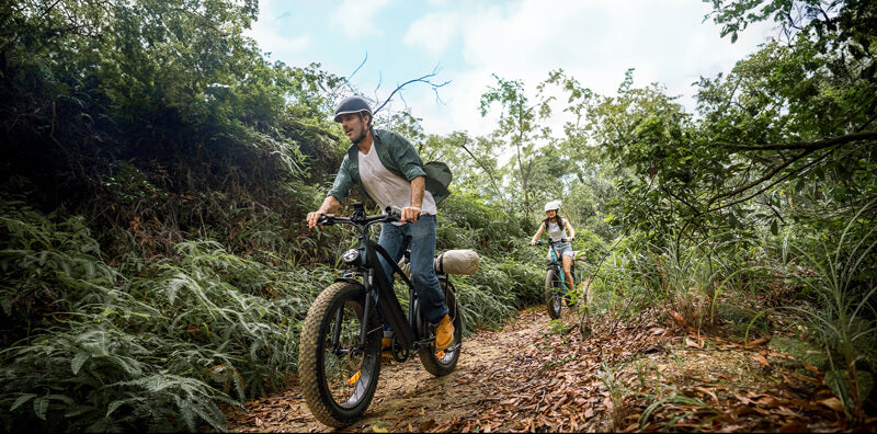 a man and a women wearing helmets ride engwe e26 e-bikes on the trail