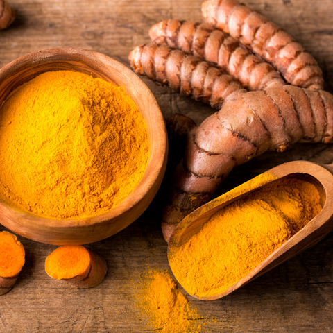 Image of turmeric root, and powder on wooden table.