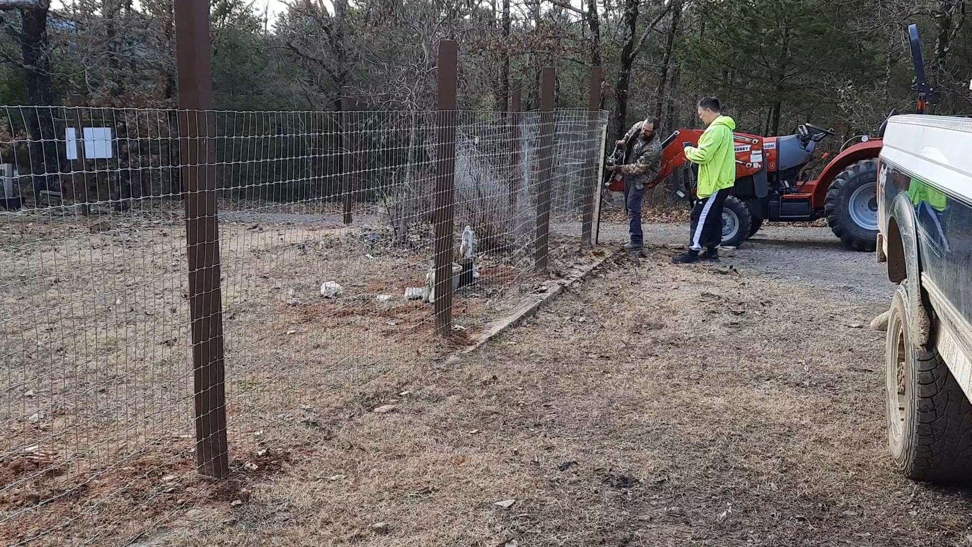 Brady and my father using a winch attached to the fence stretcher on one end, and the tractor on the other, to stretch the woven wire fence.