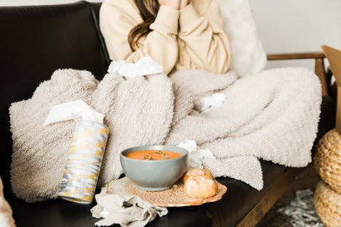 Image of girl sitting on the couch with a bowl of tomato soup and rolls. 