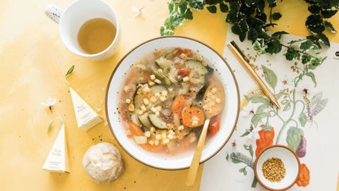 Image of Spoonful of Comfort Harvest Vegetable Soup with a cup of tea and rolls.