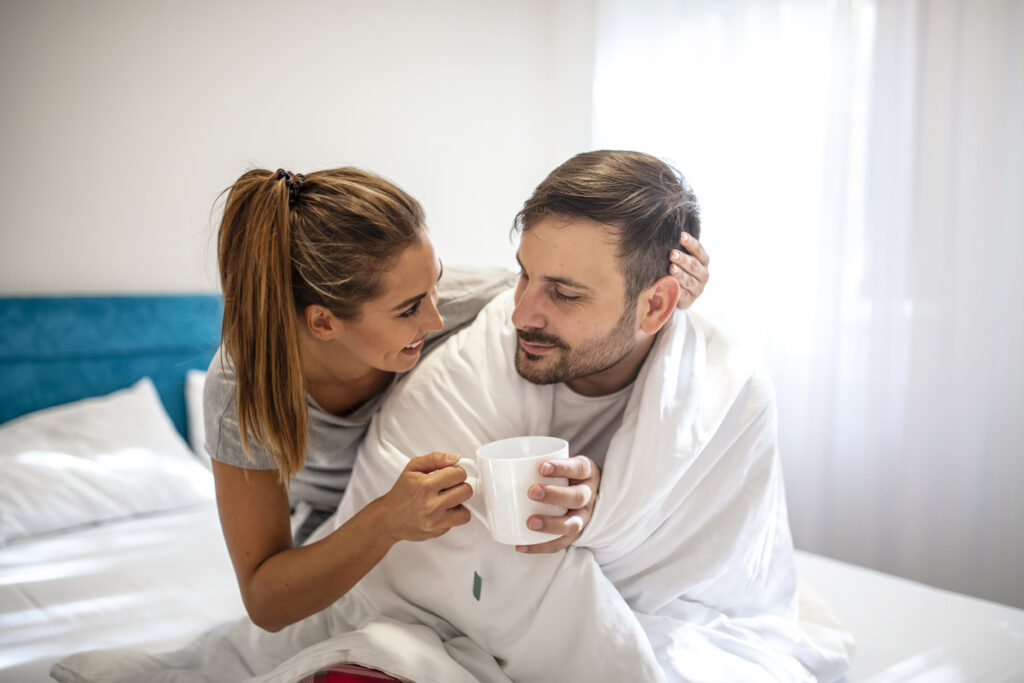 Woman touching forehead of ill husband. Woman taking care of her sick boyfriend lying on the sofa. Young woman taking care of ill man lying on couch at home