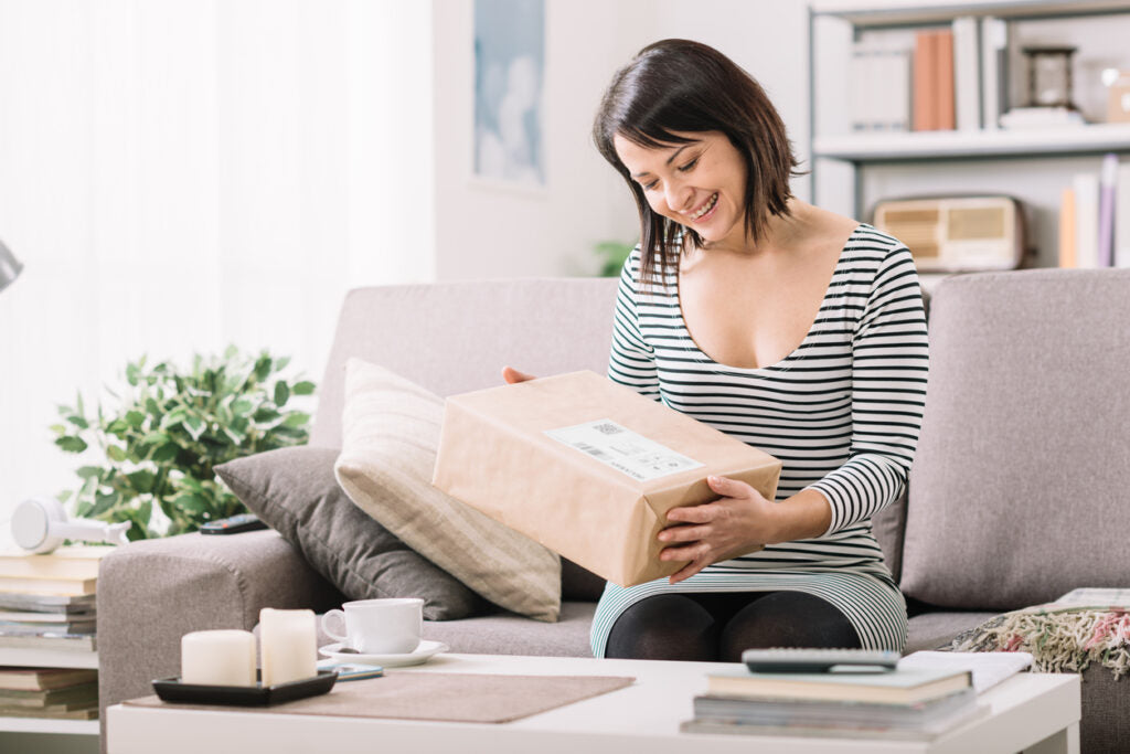 smiling young woman at home on the couch, she has received a postal parcel, online shopping and delivery concept