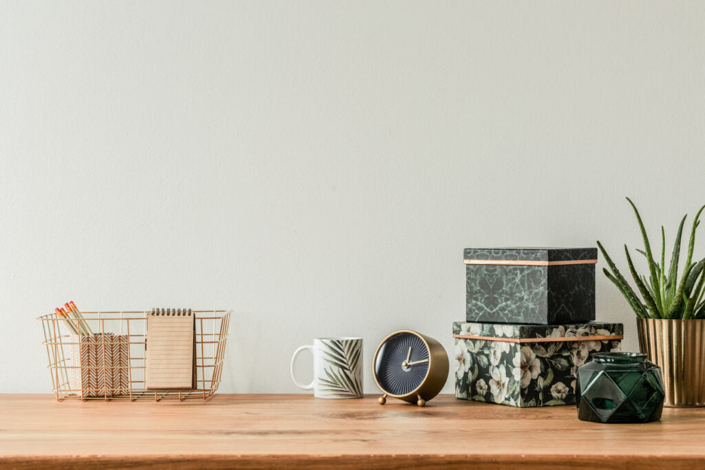 Organized table top with floral boxes, mug, clock and metal box on empty wall