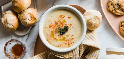Bowl of Spoonful of Comfort Poblano Chicken Chowder soup with rolls and cookies.