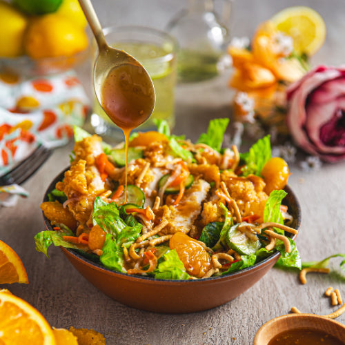 A vibrant salad topped with mandarin slices and crispy wontons, drizzled with dressing from a spoon.