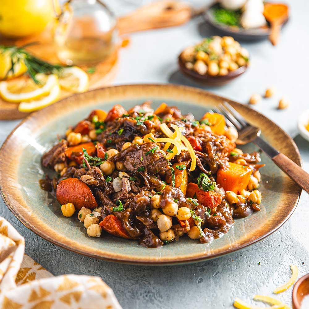 A plate of beef stew with vegetables and chickpeas, garnished with lemon zest and parsley.