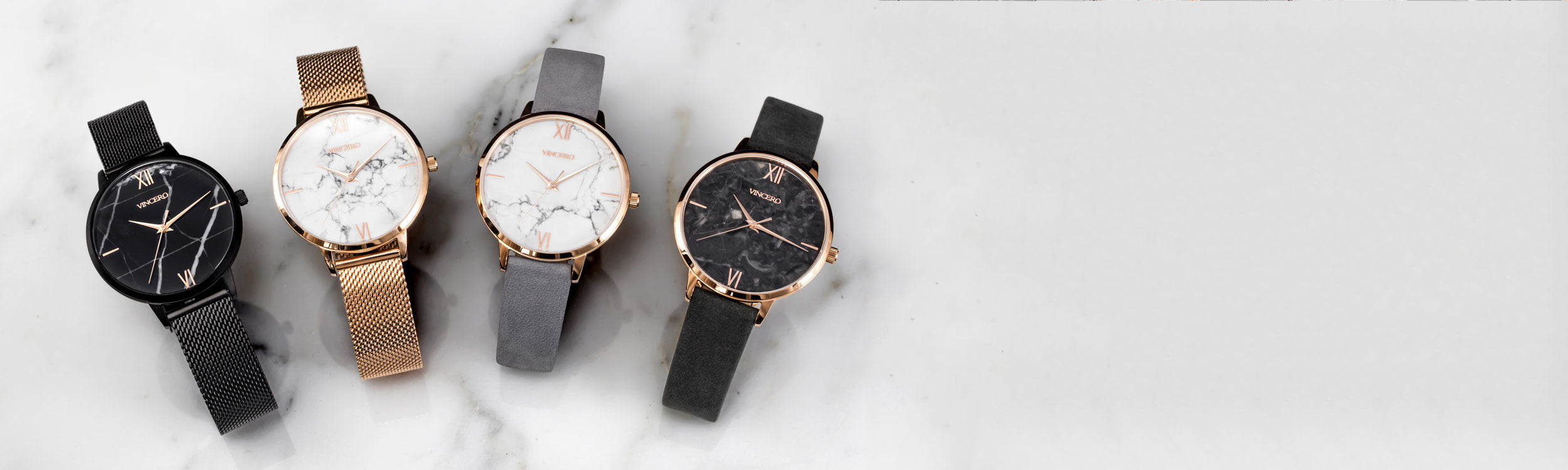 Four marble faced watches with mesh and leather straps laying in white marble