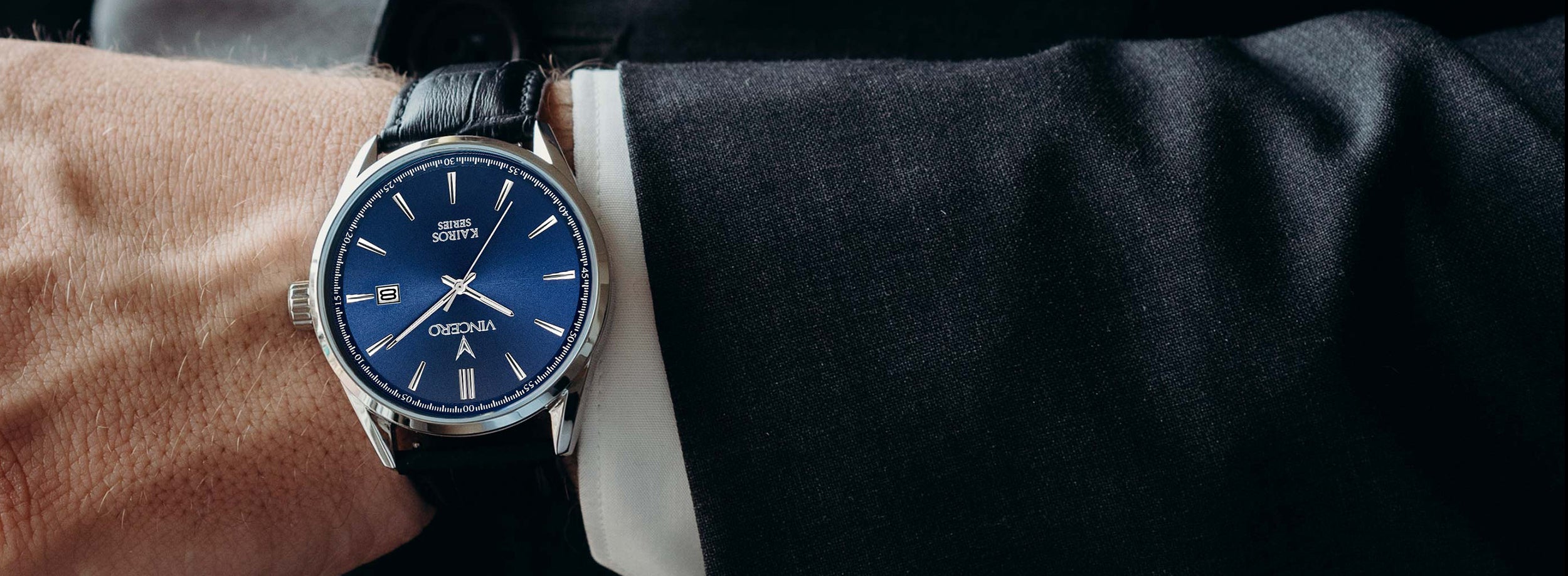 Close up of suit cuff wearing blue and silver watch with black leather strap