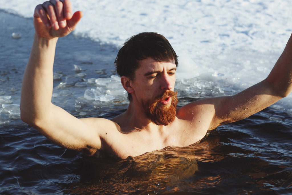 Male athlete submerged in an icy lake with his arms raised out of the water