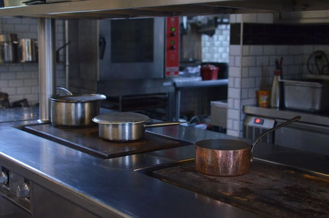 Stainless steel pan and pot and a copper pan in a commercial kitchen.